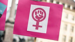 Bei einer Demonstration wird ein Schild mit dem Symbol der Frauenbewegung hochgehalten