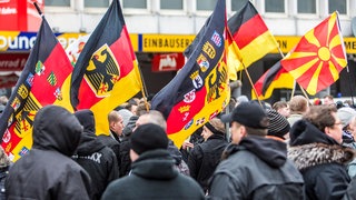 Demonstration mit schwarz gekleideten Trägern von Fahnen mit deutschen Symbolen.