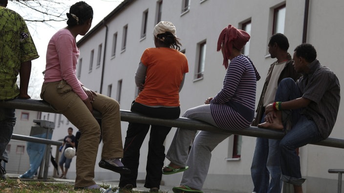 Flüchtlinge sitzen auf einem Gelände.