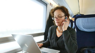 Eine junge Frau sitzt in einem Zug der Deutschen Bahn und arbeitet an ihrem Laptop.