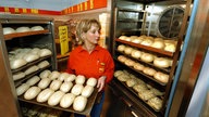 Mitarbeiterin in einem Discounter hält ein Bleck voller gebackenen Brötchen in den Händen.