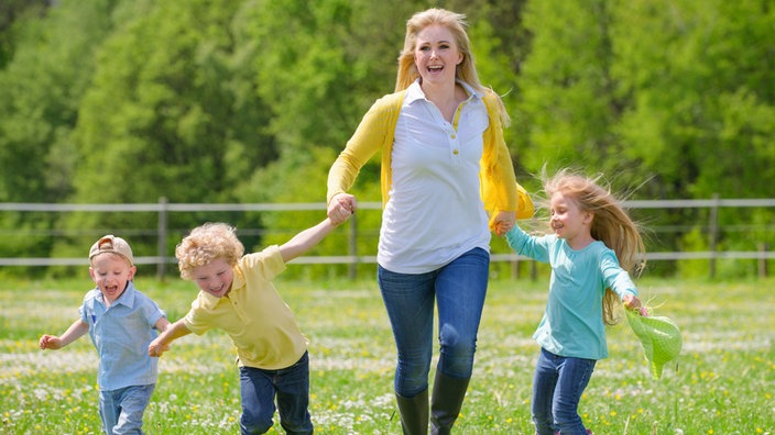 Eine Frau tobt mit drei Kindern auf ener Wiese