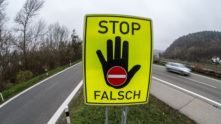 Mit den Worten Stop und Falsch sowie einer ausgestreckten Handfläche und einem Einbahnstraßen-Schild weist ein knallgelbes Verkehrsschild die Fahrzeuglenker darauf hin, nicht auf die falsche Seite der Autobahn aufzufahren.