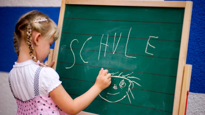 Ein kleines Mädchen schreibt auf eine Tafel