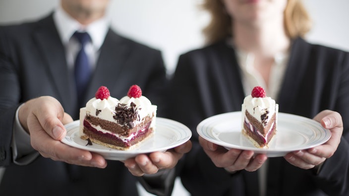 zwei Personen halten zwei unterschiedlich große Kuchenstücke auf einem Teller.