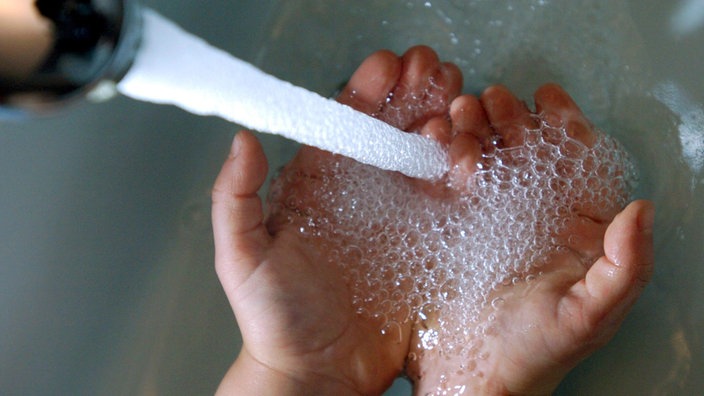 Zwei Hände, die unter einem laufenden Wasserhahn gewaschen werden.