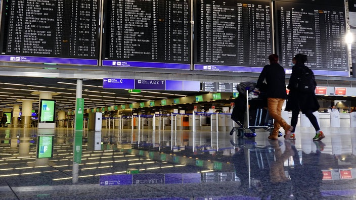 Zwei Reisende gehen an einer Flughafen-Anzeigentafel vorbei.