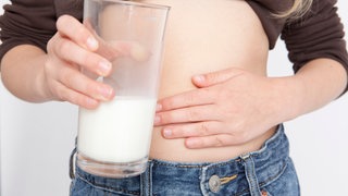 Groißaufnahme: Ein Mädchen fasst sich an den Bauch und hält in der anderen Hand ein Glas Milch