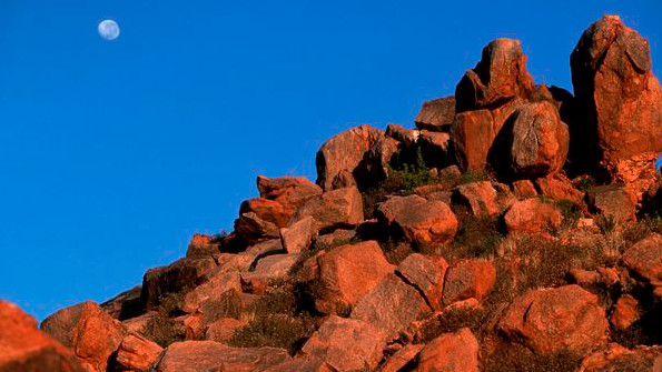 Von der untergehenden Sonne rot scheinende Felsen, auf die auf der anderen Seite der Mond scheint.