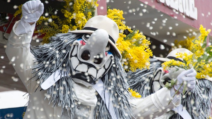 Ein verkleideter Gast der Basler Fasnacht reckt die Hände nach oben, tanzt, während es Konfetti regnet.