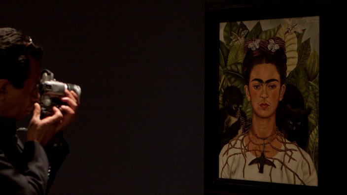 Der Besucher eines Museums macht ein Foto des Gemäldes “Selbstporträt mit Dornenkette und Kolibri“. Auf dem Gemälde ist Frida Kahlo zu sehen, die eine Dornenkette trägt, an der ein toter Kolibri hängt.