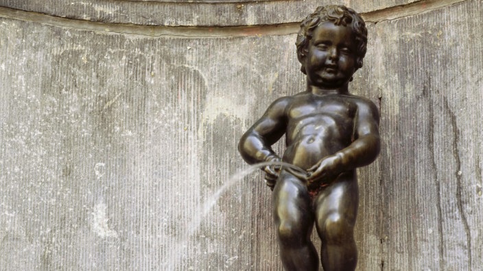 Grinsend strullt das nackte Manneken Pis auf den Betrachter herab.