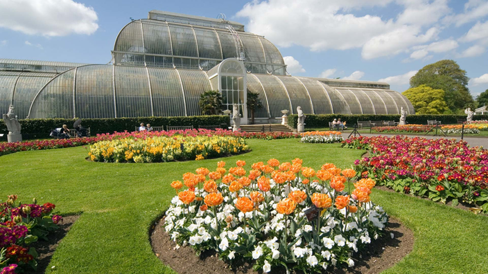 Park mit runden Beeten voller blühender Blumen und Palmenhaus.