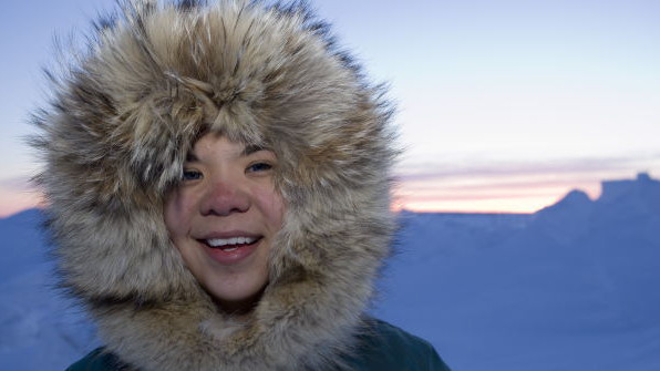 Ein Inuit-Kind lacht den Betrachter an. Sein Gesicht ist von einem dicken Pelz umrahmt.