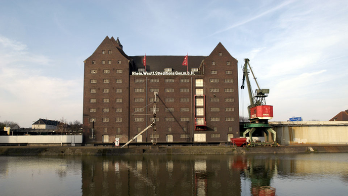 Speichergebäude aus dunklem Backstein. Davor stehen zwei Kräne.