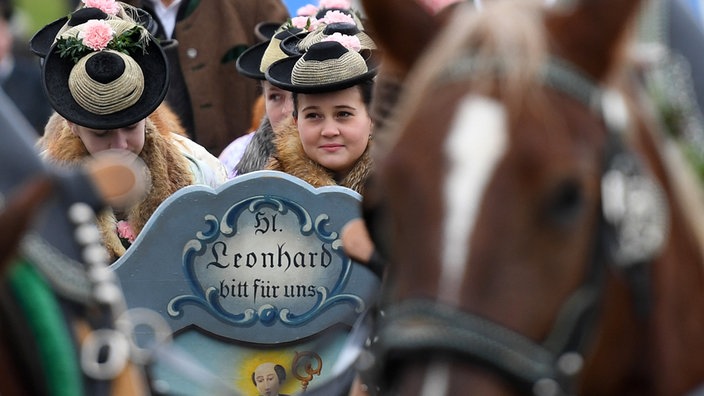 Eine Frau in Tracht hält auf einer Prozession ein Schild mit der Aufschrift "Hl. Leonhard bitt für uns"