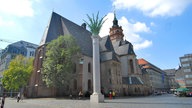 Daneben steht eine weiße Säule mit Palmwedeln am oberen Ende.