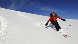 Ein Skifahrer fährt in hellem Sonnenschein auf den Betrachter zu.