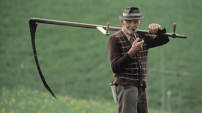 Alter Landwirt mit Sense auf der Schulter.