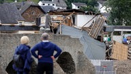 Zwei Menschen von hinten, die die Zerstörung im Ahrtal nach der "Jahrhundertflut" 2021 betrachten 