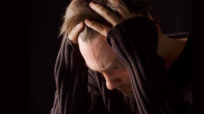 Ein Mann mit vorgebeutem Kopf, die Hände greifen in die Haare.