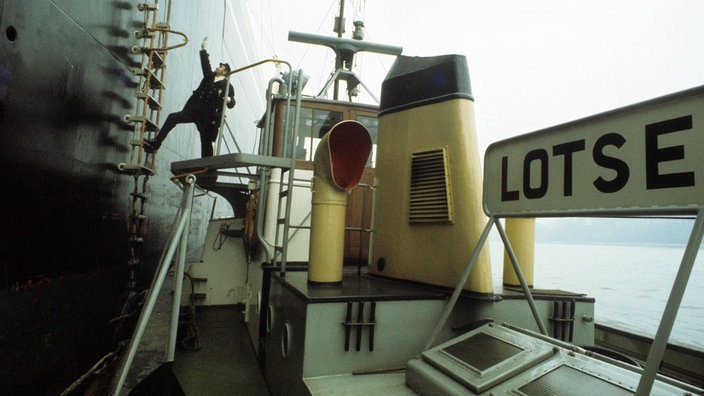 Ein Lotse besteigt von seinem Boot auf die Außenleiter eines großen Frachtschiffs 