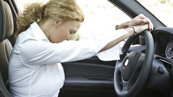 Eine Autofahrerin lehnt sich müde auf ein Lenkrad